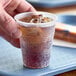 A person holding a Dart translucent plastic cup with a brown liquid and ice.