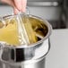 A hand holding a yellow plastic bag over a stainless steel round pan.