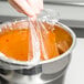 A hand using a 4 Qt. Round PTL Pan Liner to cover a bowl of soup.