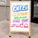 An Aarco oak A-frame sign with white marker board displaying "Check out these delicious deli items" on a sidewalk.