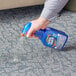 A hand holding a blue bottle of Spot Shot Professional Strength Instant Carpet Stain Remover spraying the liquid on a carpet.