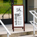 An Aarco cherry A-frame sign board with white marker board on the steps of a building.