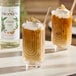 A glass of iced coffee topped with whipped cream and almond slices, with a bottle of Monin Premium Almond (Orgeat) Flavoring Syrup in the background.