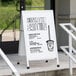 An Aarco white aluminum A-Frame sign with a drawing of a coffee cup on it.