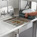 A man using a Regency stainless steel pre-rinse basket to wash dishes in a kitchen sink.