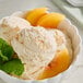 A bowl of ice cream topped with Monin Peach Fruit Puree and mint leaves.