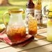 A pitcher of Monin peach iced tea on a table with glasses of ice tea.