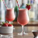 Two glasses of Monin strawberry drink with straws and a strawberry.