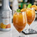 Two glasses of mango liquid with mint leaves and orange slices on a table.