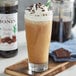 A glass of Monin chocolate fudge flavoring syrup in brown liquid with whipped cream and chocolate sprinkles.