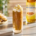 A tall glass of iced coffee topped with whipped cream and caramel syrup, with a bottle of Monin Sugar-Free Caramel Flavoring Syrup in the background.