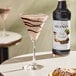 A bottle of Monin Premium Dark Chocolate Flavoring Syrup next to a chocolate martini in a cocktail glass.