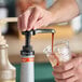 A hand pressing a Monin puree pump to dispense syrup into a plastic cup with ice.
