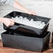 A person holding a black container with ice in it.