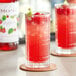 A glass of Monin raspberry fruit syrup mixed with red liquid garnished with mint on a table in a cocktail bar.