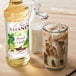 A bottle of Monin Premium French Vanilla Flavoring Syrup next to a glass of milk and a glass of iced coffee.