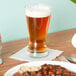 A Libbey pilsner glass of beer next to a plate of food.