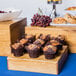 A Cal-Mil Madera rustic pine square riser on a table with a group of muffins in brown wrappers.