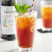 A glass of iced tea with a straw and mint leaves, flavored with Monin Premium Sugarcane Cola Flavoring Syrup.