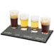 A Cal-Mil faux slate tray with beer glasses filled with brown and dark liquid on a table.