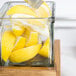 A person slicing lemons into a glass jar on a counter.