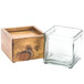 A wooden box with a hole in the middle holding a square glass jar with a wooden lid.