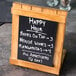 A Cal-Mil Madera chalkboard stand with a happy hour sign on a table.