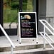 An Aarco aluminum A-frame sign board with a black marker board displaying "Taco" on a sidewalk.