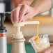 A hand pressing a Monin flavoring sauce pump to dispense sauce into a cup of ice.
