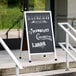 An Aarco black chalkboard A-Frame sign on a sidewalk.