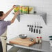 A woman in an apron using a Regency stainless steel wall shelf to put food in a can.