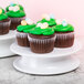 A group of Elite Global Solutions white melamine plates with Easter cupcakes with green frosting and candy eggs on top.