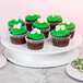 An Elite Global Solutions white melamine plate on a pedestal with cupcakes frosted with green and candy eggs on it.