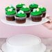 A hand holding an Elite Global Solutions white melamine plate with cupcakes topped with green frosting and candy.