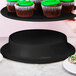 A person holding a black Elite Global Solutions melamine pedestal with cupcakes on it.