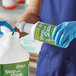 A person in blue gloves pouring Noble Chemical Step and Shine floor cleaner from a white bottle into a green container.