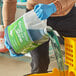 A person pouring Noble Chemical floor cleaner from a green jug into a yellow container.