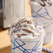 A clear plastic dome lid with a 2-inch hole, fitted on a paper cup filled with a whipped cream and chocolate-topped beverage.