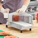 A commercial tomato slicer with a metal frame and multiple blades, designed for quickly slicing tomatoes.