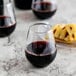 A close up of a Fineline clear plastic stemless wine goblet filled with red wine next to a plate of pineapples.