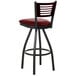 A BFM Seating black metal bar stool with a mahogany wood back and red vinyl seat.