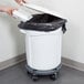 A person's hand putting a white lid on a Rubbermaid white trash can.