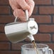 A hand using a Vollrath Triennium stainless steel coffee pot to pour coffee into a glass.