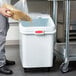 A person putting food into a white Rubbermaid ingredient bin with a scoop.