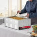 A woman in a chef's uniform using tongs to serve food from a container in an Avantco countertop food warmer.