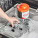 A hand using a Noble Products glass washer brush to clean a glass in a sink.