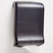 A black M-Fold paper towel dispenser on a white tile wall.