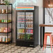 A black refrigerated sliding glass door merchandiser with LED lighting, stocked with various beverages.