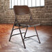 A brown National Public Seating metal folding chair in front of a brick wall.