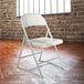 A gray National Public Seating Commercialine metal folding chair in front of a brick wall.